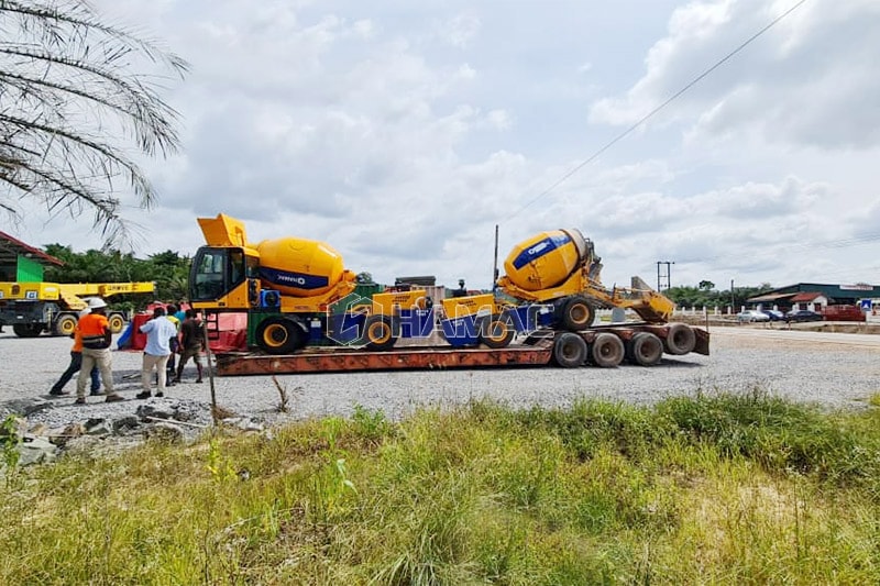 Dua mixer beton swa-muat dimuat di trailer rendah untuk pengangkutan ke lokasi kerja lainnya.